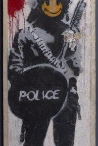 Banksy artwork of a riot police officer with a yellow smiley face at Moco.